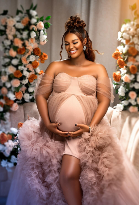 Radiant pregnant woman in a flowing pink gown, surrounded by flowers, captured by black photographers in Columbus, Ohio, specializing in family and maternity photography in Ohio.