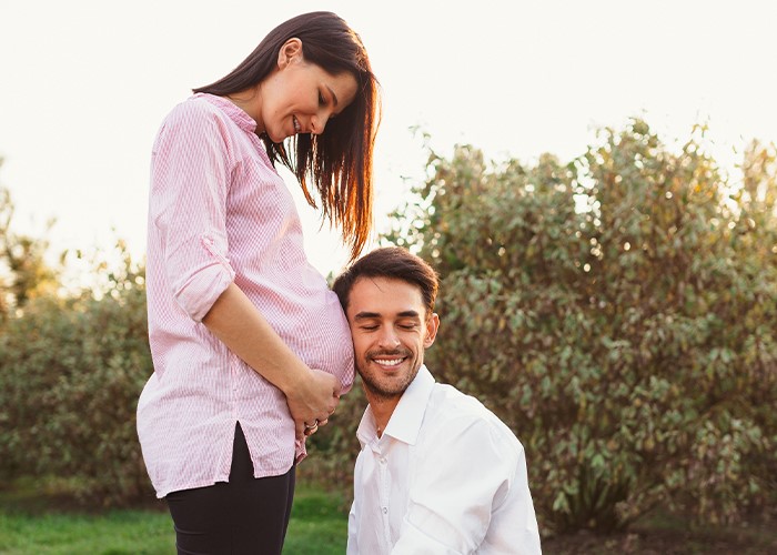 Happy couple enjoying a moment in a garden with the expectant mother gently cradling her baby bump while her partner lovingly smiles at her in the early evening light.