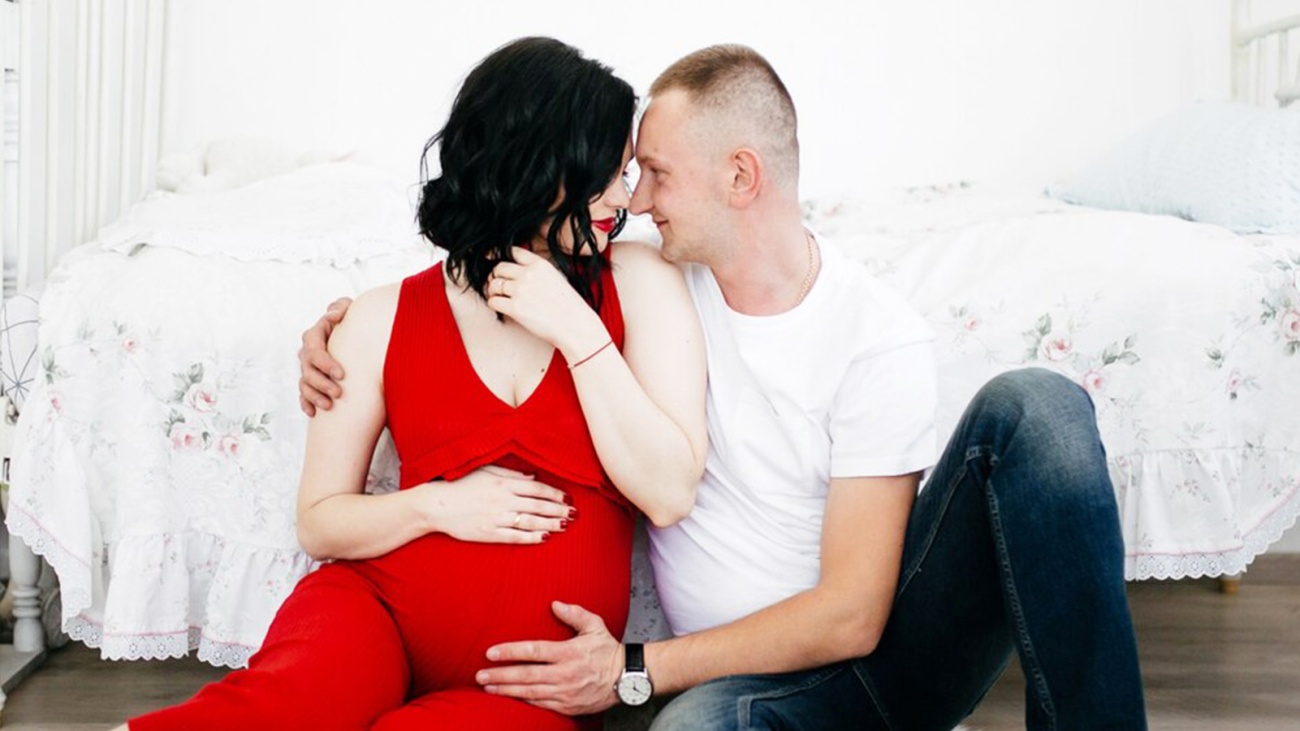 Expecting couple sitting on floor in cozy room woman wearing red dress while man in white shirt embraces her lovingly family joy and anticipation of new life together