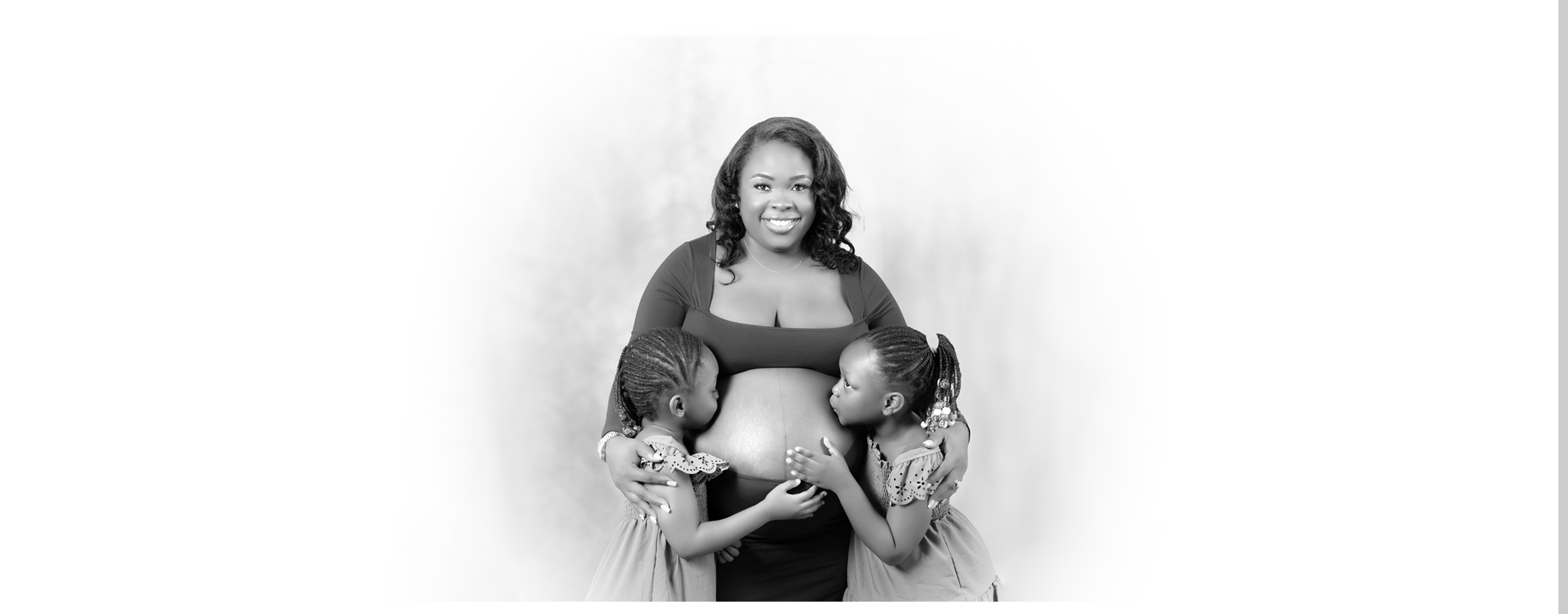 A joyful and heartwarming black and white maternity portrait of a smiling pregnant woman with two young children lovingly embracing her baby bump, symbolizing family love.