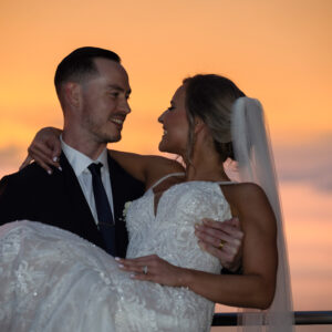 Bride and groom embrace during sunset wedding portrait sharing joyful smiles with romantic orange sky backdrop capturing the essence of their special day
