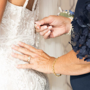 A close-up of a woman's hands delicately buttoning or adjusting the back of an elegant lace wedding dress creating a special moment before the wedding ceremony.