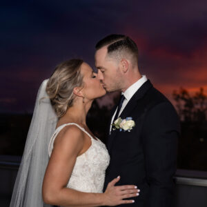 Bride and groom share a romantic kiss at sunset captured in a stunning wedding portrait showcasing love and elegance against a breathtaking evening sky background.