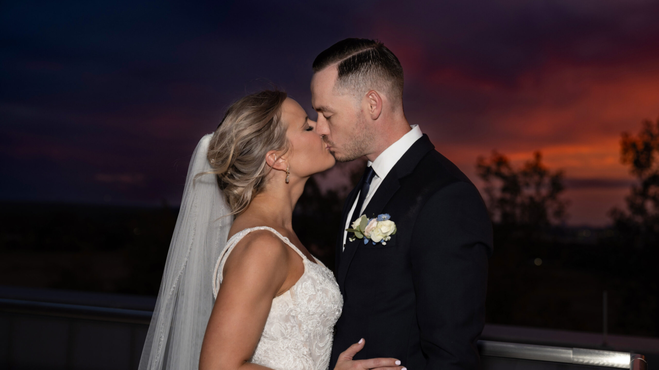 Bride and groom share a romantic kiss at sunset captured in a stunning wedding portrait showcasing love and elegance against a breathtaking evening sky background.