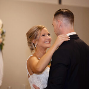 A bride and groom share a joyful first dance at their wedding reception surrounded by elegant decor featuring a floral wreath and soft lighting.