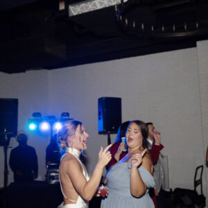 Guests joyfully dancing at a lively party or celebration with colorful lights and a DJ setup in the background creating a festive and energetic atmosphere.