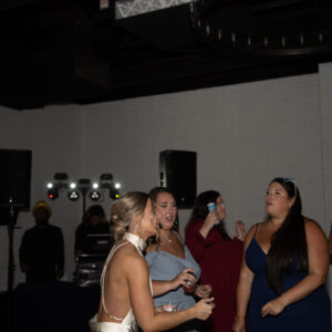 People enjoying themselves at a lively party in a dimly lit venue with a DJ booth in the background and colorful dresses creating a vibrant atmosphere.