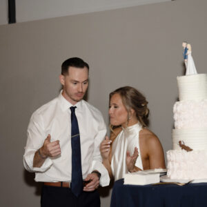 A couple celebrating their wedding with a three-tiered cake. The bride and groom are dressed elegantly, sharing a special moment next to the beautifully decorated dessert.