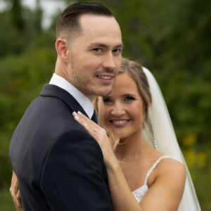 Bride and groom embracing on their wedding day with a natural outdoor background showcasing love and happiness with the bride smiling behind the groom dressed in formal attire.
