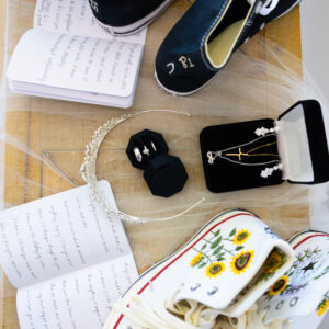 Wedding preparation with personalized sneakers, handwritten vows, floral bouquet, and jewelry displayed, showcasing unique and stylish bridal accessories.