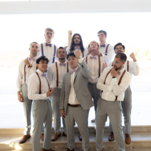 A group of groomsmen in coordinated attire including gray suits and white shirts pose together in a brightly lit room highlighting camaraderie and wedding celebration.