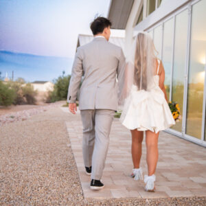 Bride and groom walk hand in hand along a picturesque path beside a modern building after their wedding ceremony showcasing love and commitment in a serene setting.