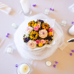 Elegant white wedding table setting adorned with candles and a floral centerpiece featuring colorful roses and small flowers creating a romantic and festive atmosphere