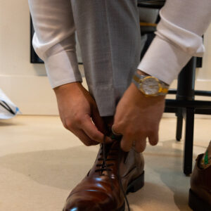 A person in formal attire tying brown leather dress shoes showcasing elegant style and attention to detail in a sophisticated setting perfect for business or special occasions.