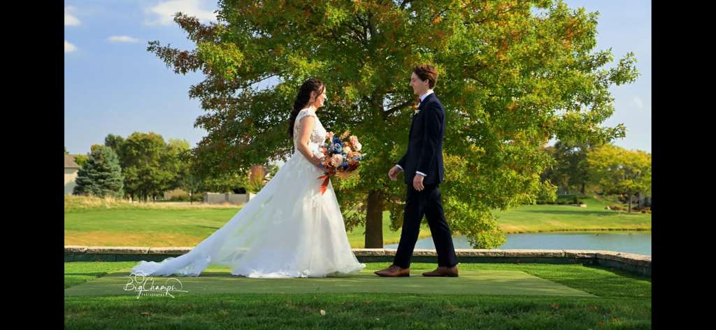 Bride and groom share a moment on their wedding day in a scenic outdoor setting with lush green trees and blue sky creating a picturesque backdrop to their celebration