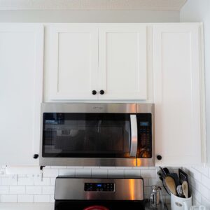 Modern kitchen with white cabinets and built-in stainless steel microwave above a stove. Bright and clean design with tiled backsplash and utensil holder on the counter.