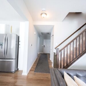 Modern home interior with stainless steel fridge, hardwood floors, and a staircase leading to the upper floor. Brightly lit hallway with contemporary design elements.