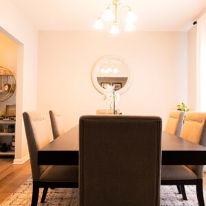 Elegant dining room with a modern dark wood table and six upholstered chairs warm lighting and a round mirror on the wall creating a cozy atmosphere for gatherings.