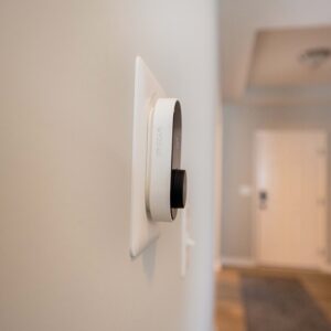 Smart thermostat mounted on a beige wall in a modern home hallway with white trim. Energy-efficient device for controlling home temperature. Cozy and inviting interior design.