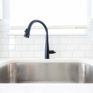 Modern kitchen with a stainless steel sink and a sleek black faucet against a white subway tile backsplash. Clean and bright design emphasizing minimalism and functionality.