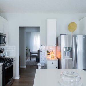 Modern kitchen interior featuring white cabinets stainless steel appliances and wooden flooring with a cozy dining area in the background offering a stylish atmosphere