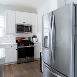 Modern kitchen with stainless steel appliances including a refrigerator oven and microwave White cabinets and subway tile backsplash enhance the sleek design