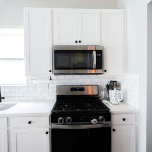 Modern kitchen with white cabinets black countertop stainless steel microwave and stove. Bright light from window enhances the clean minimalist design.