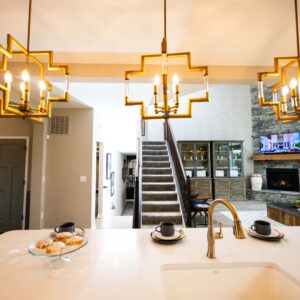 Modern kitchen interior featuring elegant lighting fixtures over a marble island with two cups and a plate of pastries stairs leading to the living area with a fireplace.