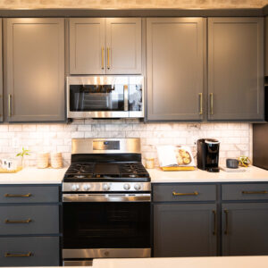 Modern kitchen with gray cabinets and stainless steel appliances including a microwave oven and refrigerator. Bright subway tile backsplash adds a clean touch.