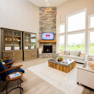 Spacious modern living room with a stone fireplace, large windows offering natural light, stylish furniture, and a cozy ambiance perfect for relaxation and entertaining.