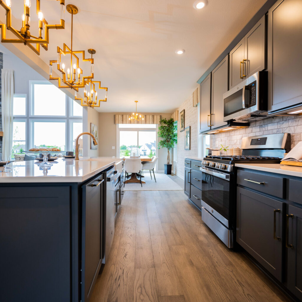 Modern kitchen interior with sleek dark cabinets and stainless steel appliances under warm lighting. Bright and spacious design with a view of the dining area.