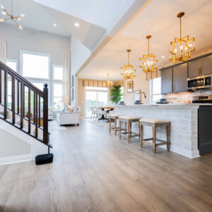 Spacious modern kitchen and dining area with sleek design featuring hardwood floors and elegant lighting adjacent to a cozy living room with large windows and decor.