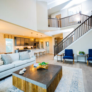 Spacious modern living room with elegant decor featuring a white sofa large coffee table open kitchen with island seating and stylish wooden staircase. Bright airy ambiance.