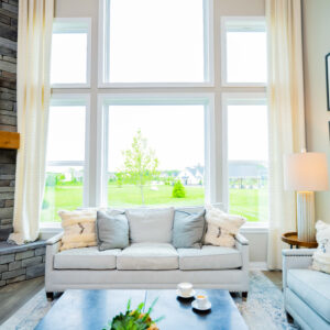 Bright and spacious living room with large windows and modern decor featuring a cozy white sofa a stone fireplace with a TV above it and a coffee table with candles