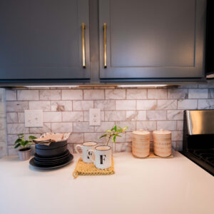 Modern kitchen countertop with elegant gray cabinets and subway tile backsplash. Features stainless steel appliances and decorative coffee mugs adding a cozy touch.