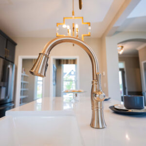 Modern kitchen interior with a gold finish faucet on a white countertop, surrounded by sleek cabinets and stylish lighting, creating a luxurious and functional space.
