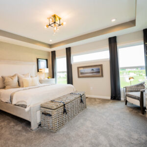Modern bedroom featuring a plush bed with neutral-toned bedding two wicker baskets carpeted floor large windows and elegant decor creating a cozy and inviting ambiance