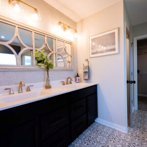 Modern bathroom with elegant black double vanity, large decorative mirror, and stylish lighting on a patterned tile floor. Clean and sophisticated interior design.