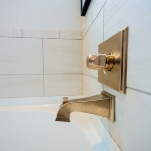 Close-up of modern bathroom faucet and handle in brushed nickel finish mounted on a white tiled wall above a bathtub offering a sleek and elegant bathroom fixture design.