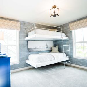 Modern bedroom with gray wooden walls featuring a stylish white bunk bed and natural light from large windows providing a cozy and inviting atmosphere.