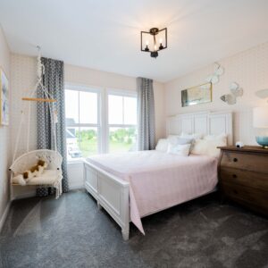 Modern bedroom with a cozy white bed and elegant decor including a wooden dresser and hanging chair by a large window. Soft lighting creates a peaceful ambiance.