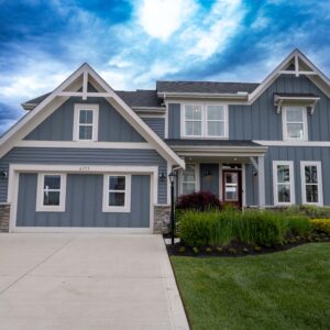 Modern suburban home with blue siding and white trim featuring a spacious driveway and well-maintained lawn under a vibrant cloudy sky. Ideal real estate property.
