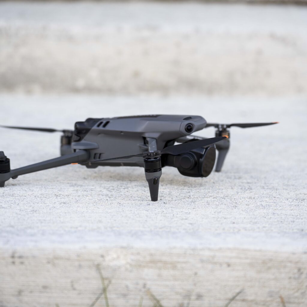 A compact black drone with propellers extended is positioned on a concrete surface outdoors, ready for flight. Ideal for aerial photography and remote exploration.