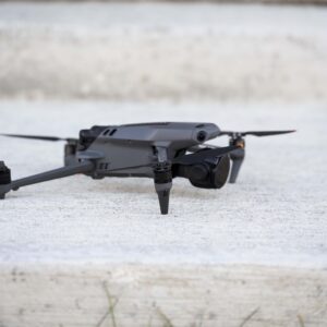 A compact black drone with propellers extended is positioned on a concrete surface outdoors, ready for flight. Ideal for aerial photography and remote exploration.