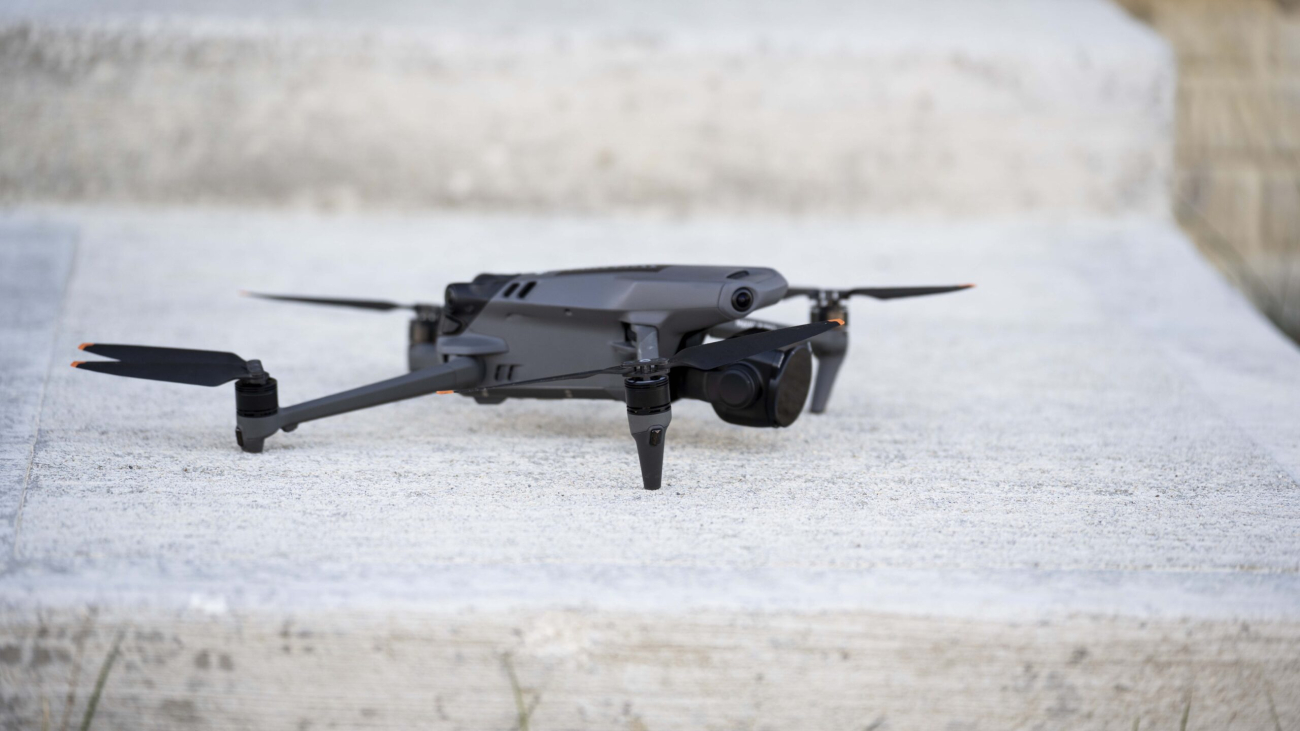 A compact black drone with propellers extended is positioned on a concrete surface outdoors, ready for flight. Ideal for aerial photography and remote exploration.