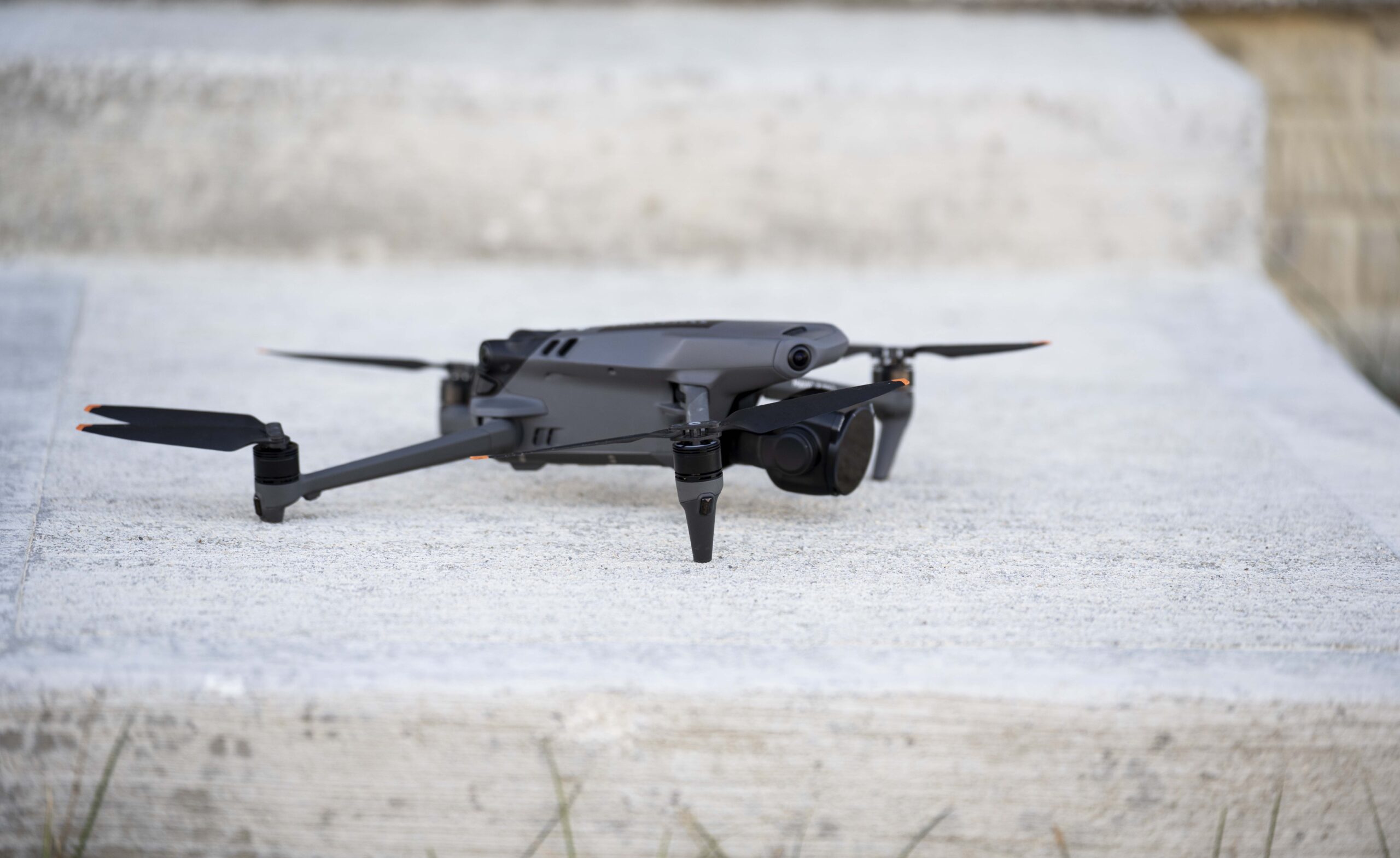 A compact black drone with propellers extended is positioned on a concrete surface outdoors, ready for flight. Ideal for aerial photography and remote exploration.