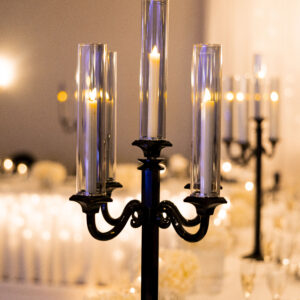 Elegant black candle holder with tall glass encasing and lit candles on a beautifully set dining table with white flowers creating a sophisticated and warm atmosphere.