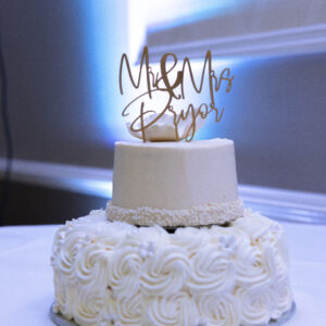 Elegant two-tier white wedding cake featuring intricate icing designs and a decorative topper under soft event lighting perfect for weddings and celebrations