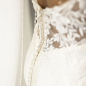 Elegant close-up of a wedding dress showcasing intricate lace details and delicate buttons on a sheer back design emphasizing bridal fashion and style.