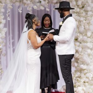 Bride and groom exchanging vows during an elegant wedding ceremony with a floral backdrop and officiant, highlighting love and commitment on their special day.